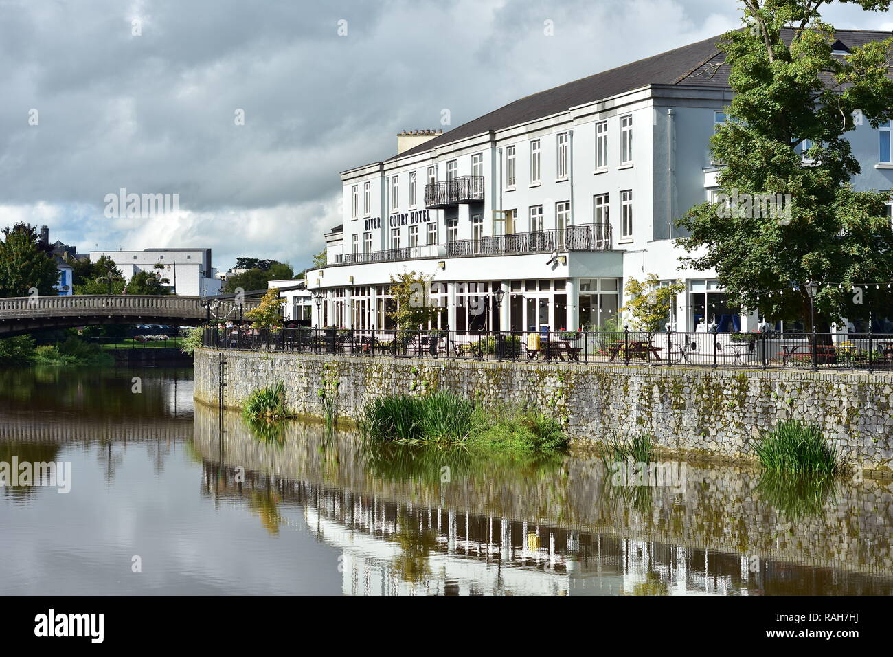 White hotel building on bank of river Nore in Kilkenny reflecting on mirror calm surface on cloudy day. Stock Photo