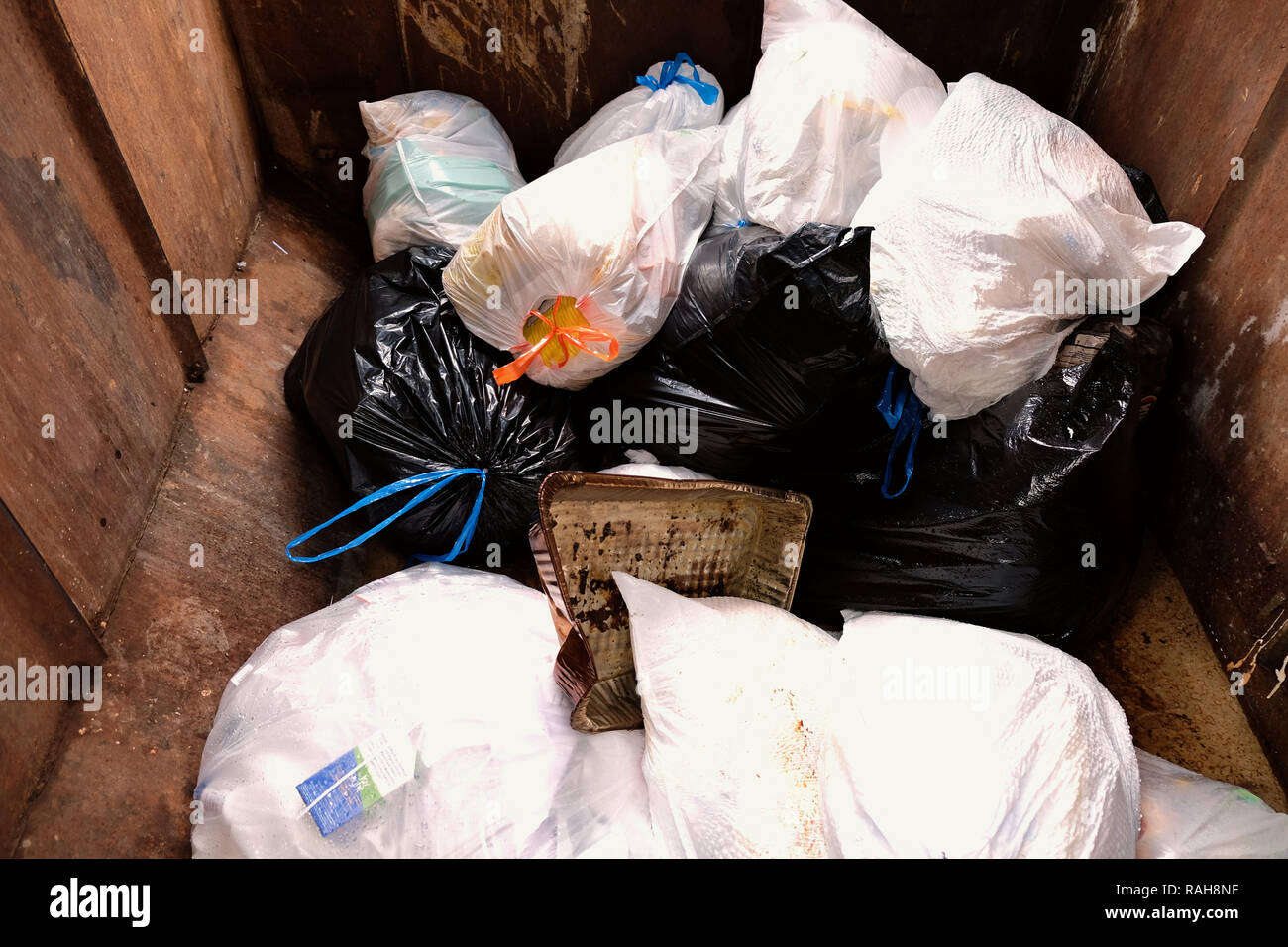 Dumpster with filled white and black trash bags; rubbish bin, rubbish
