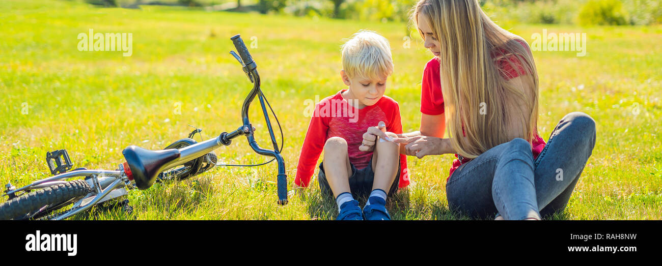 The boy fell off the bicycle, his mother pastes a plaster on his knee BANNER, LONG FORMAT Stock Photo
