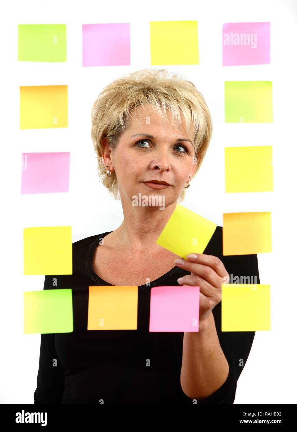 Woman sticking PostIt sticky notes to a sheet of glass Stock Photo