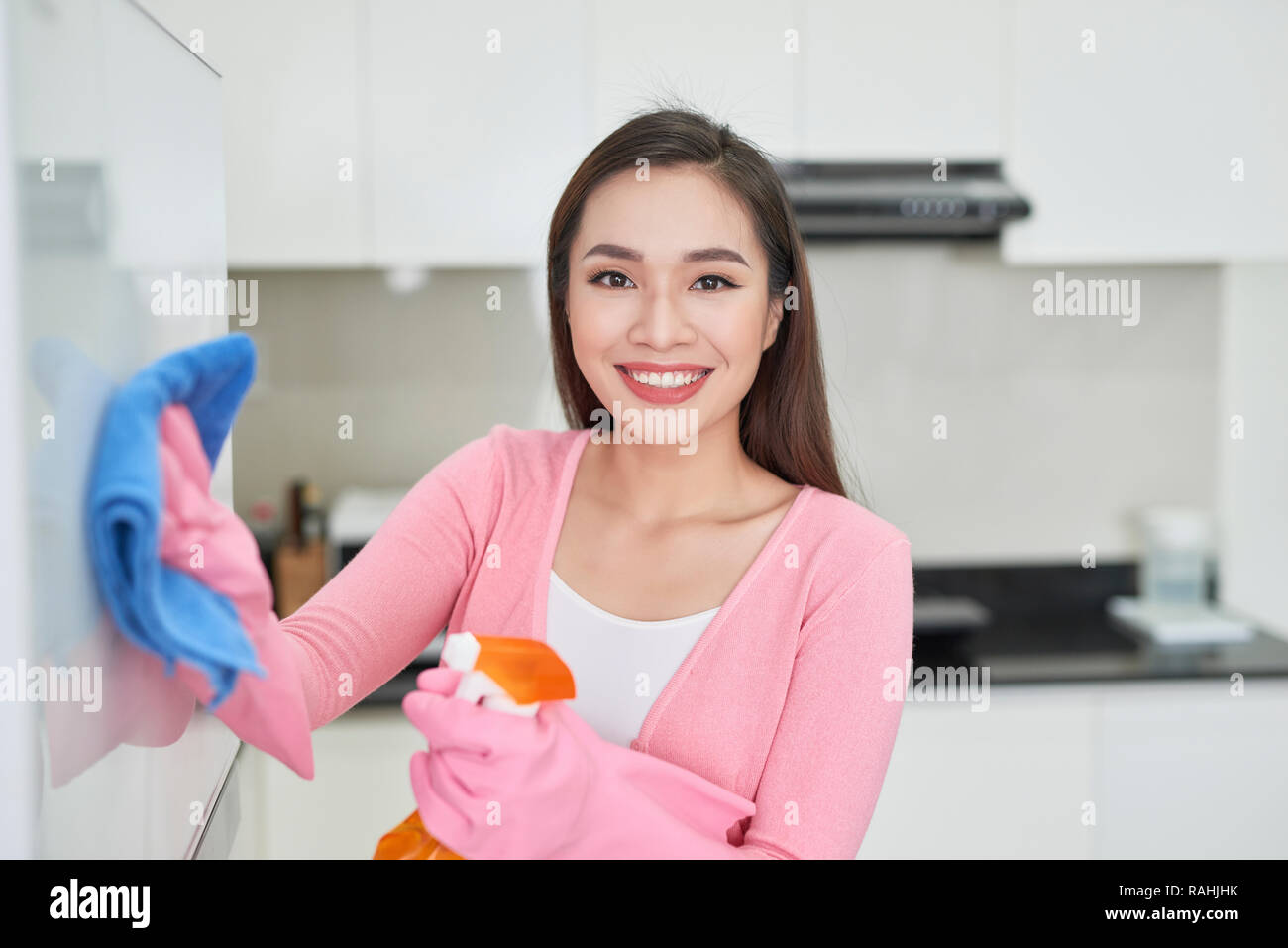 Woman in protective gloves cleaning refrigerator with rag indoors Stock Photo