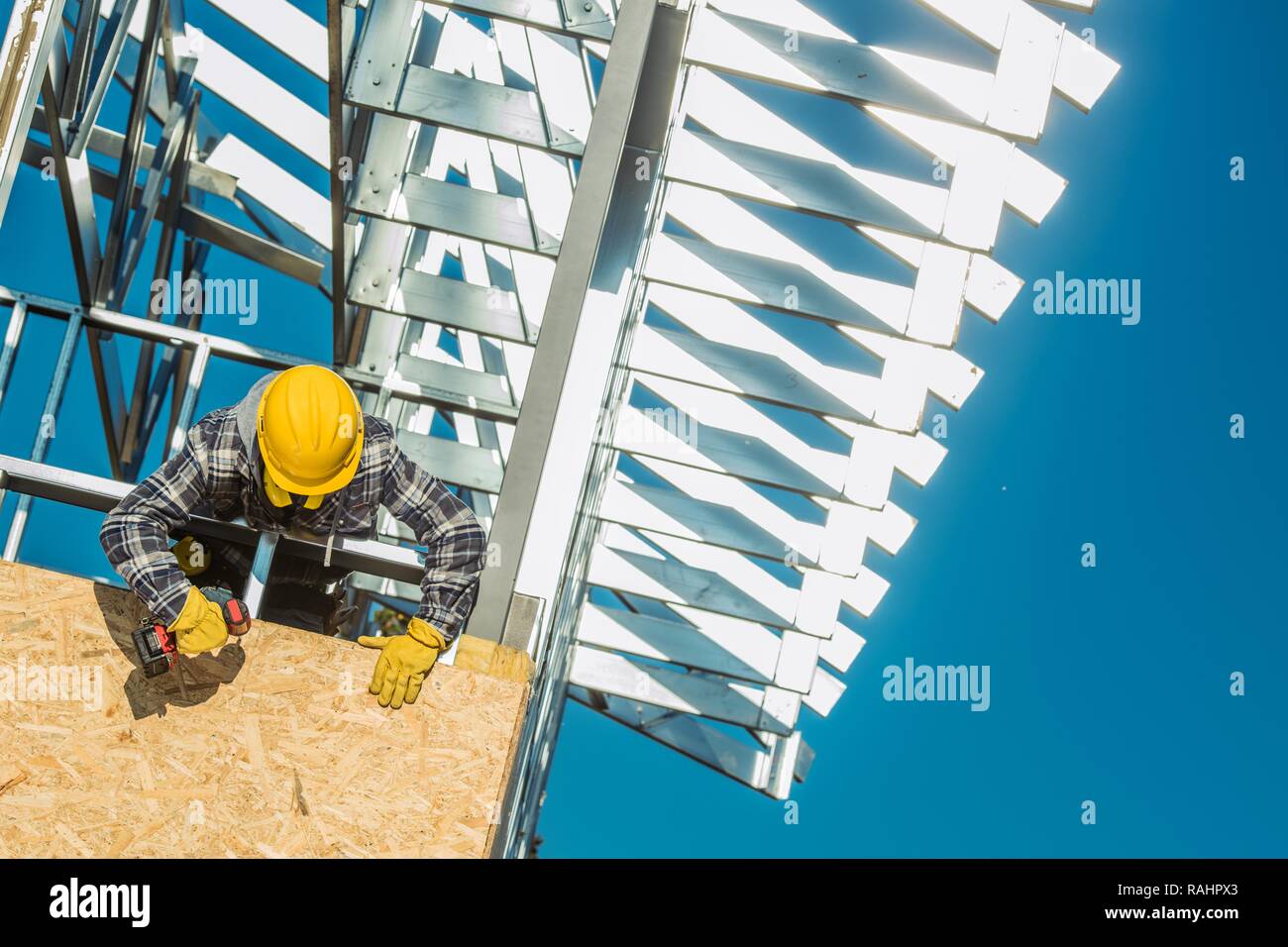 Skeleton Frame Home Construction Worker in Yellow Helmet Installing Metal Elements. Construction Industry Theme. Stock Photo
