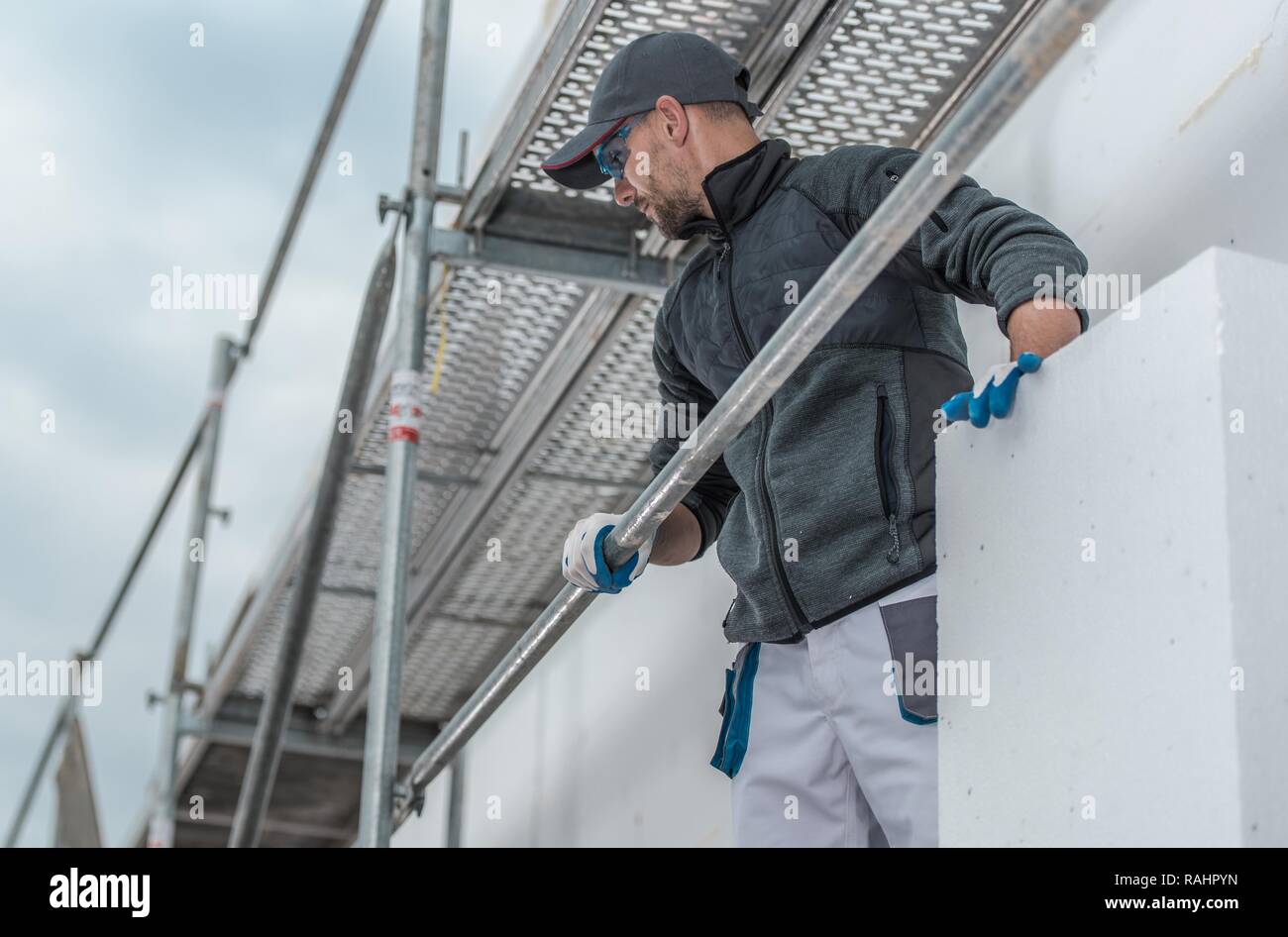 Building Insulating From Scaffolding. Caucasian Construction Worker with Insulation Material in Hands. Stock Photo