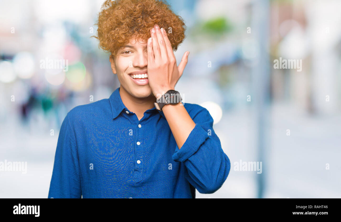 Young handsome elegant man with afro hair covering one eye with hand