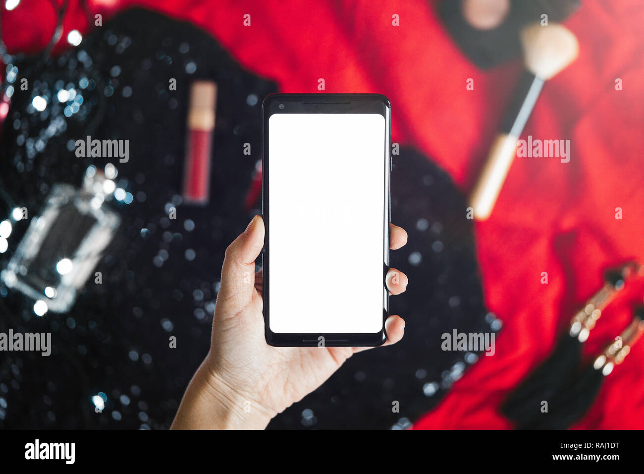 Close up of hand holding mobile phone with blank screen above cocktail dress. Stock Photo