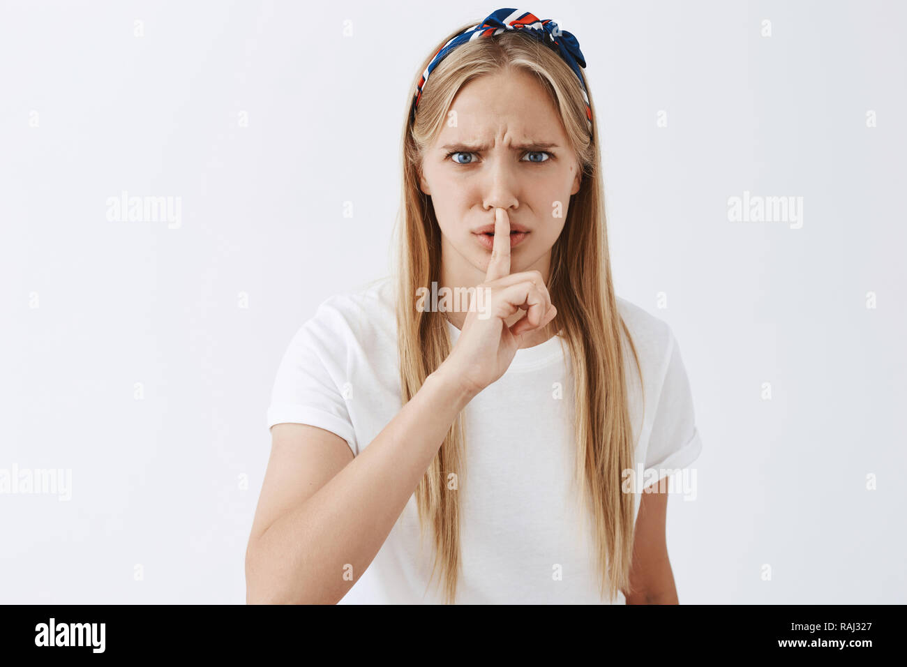 How can you say that, shut up. Angry and upset european fair-haired woman shushing at man showing disrespect, being disappointed and outraged, showing shh gesture with index finger over mouth Stock Photo