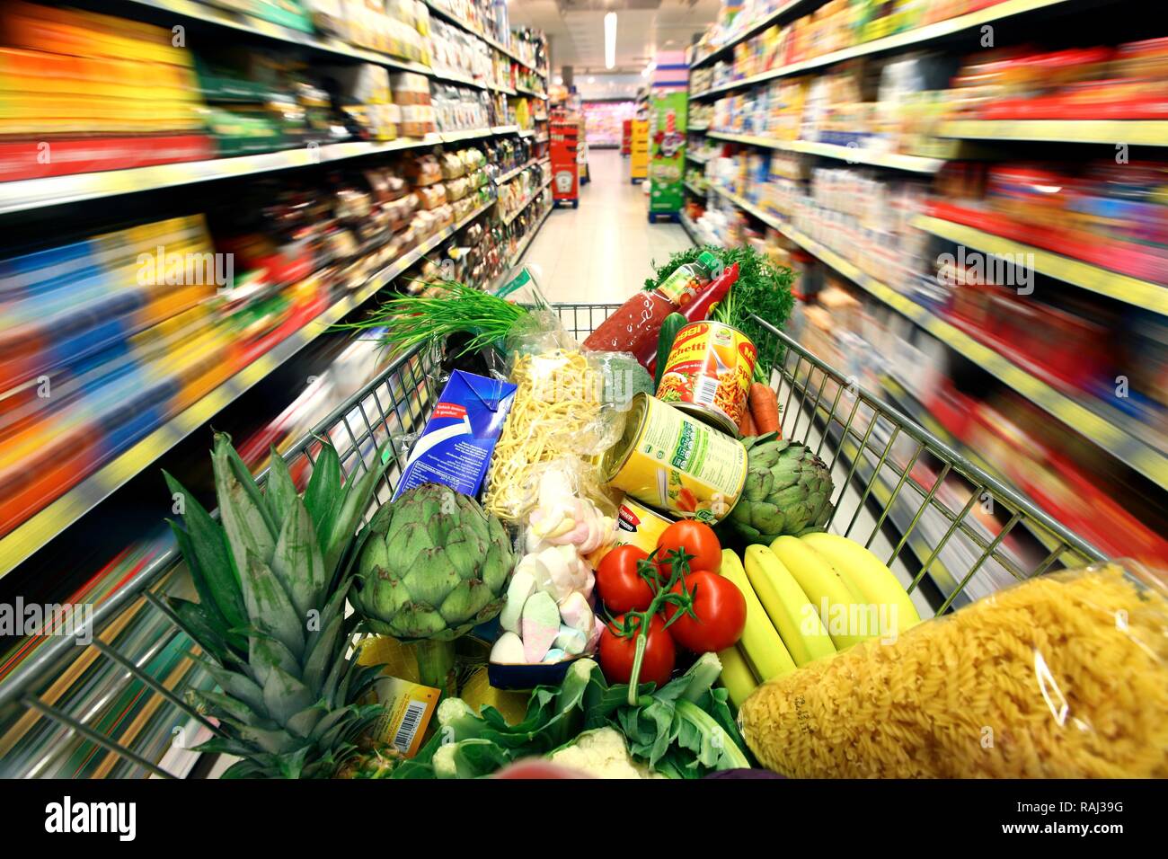 Full shopping trolley being pushed down the aisle, food hall, supermarket Stock Photo