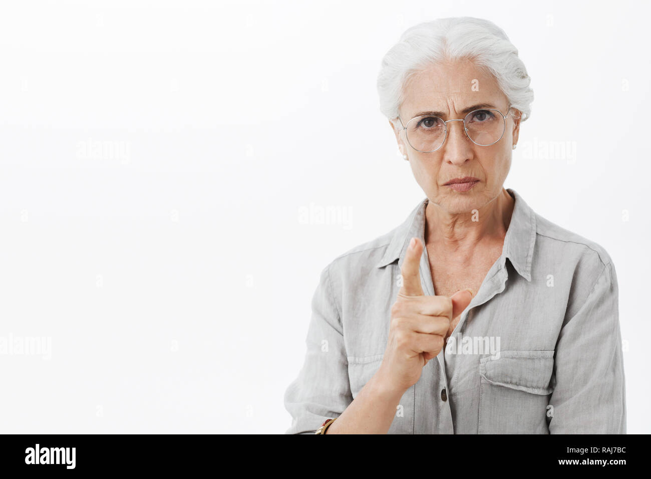 I forbid you. Portrait of strict and serious disappointed granny with white hair in glasses frowning with mad expression shaking index finger in scolding and prohibition, warning kid to be nice Stock Photo
