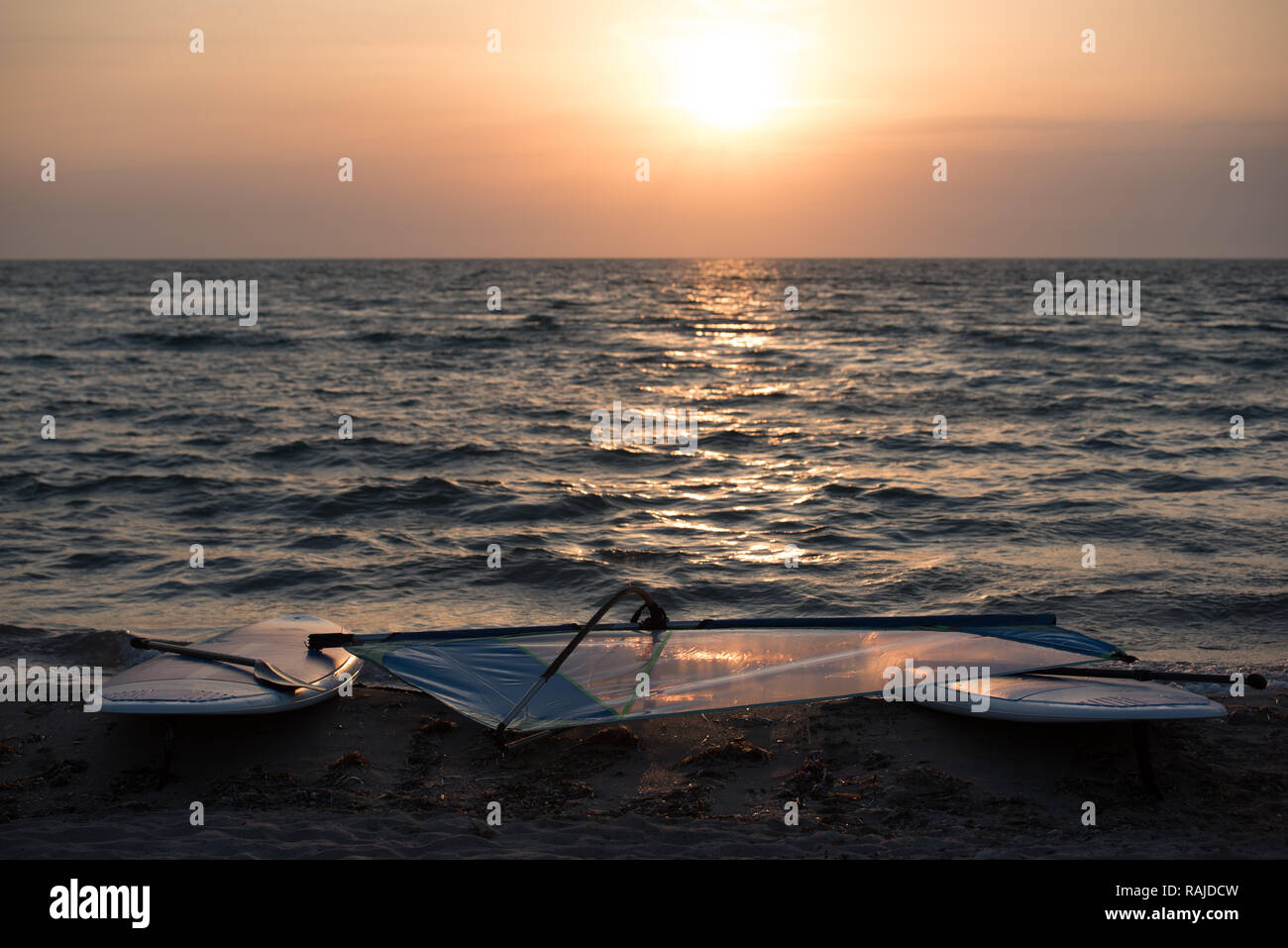 Landscape of sandy beach with windsurfing boards lying on background of sea in sunset light. Stock Photo