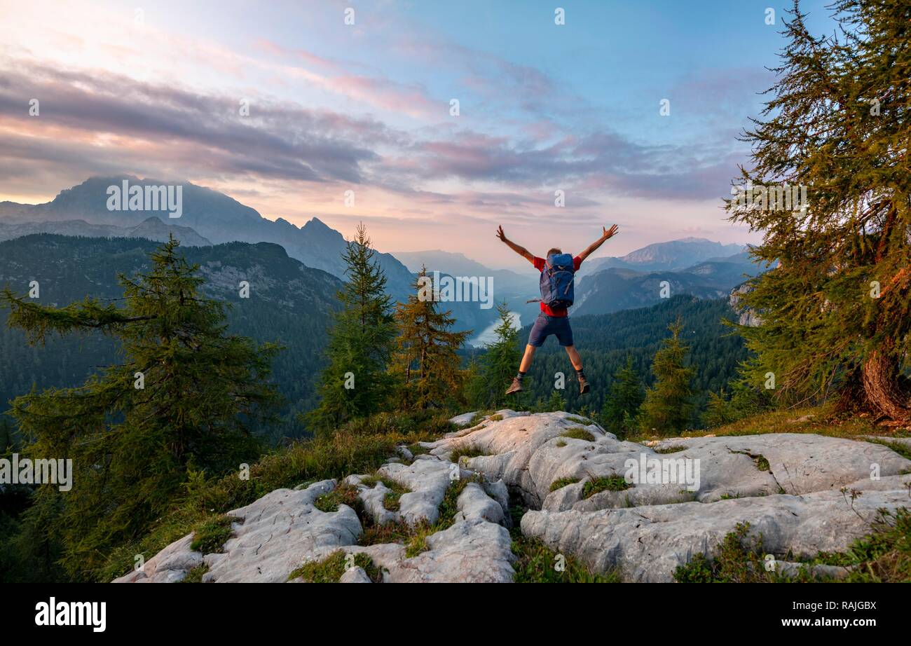 Hiker jumps, summit of Feldkogel, view of Königssee at sunset, left Watzmann Südspitze and Watzmannkinder Stock Photo