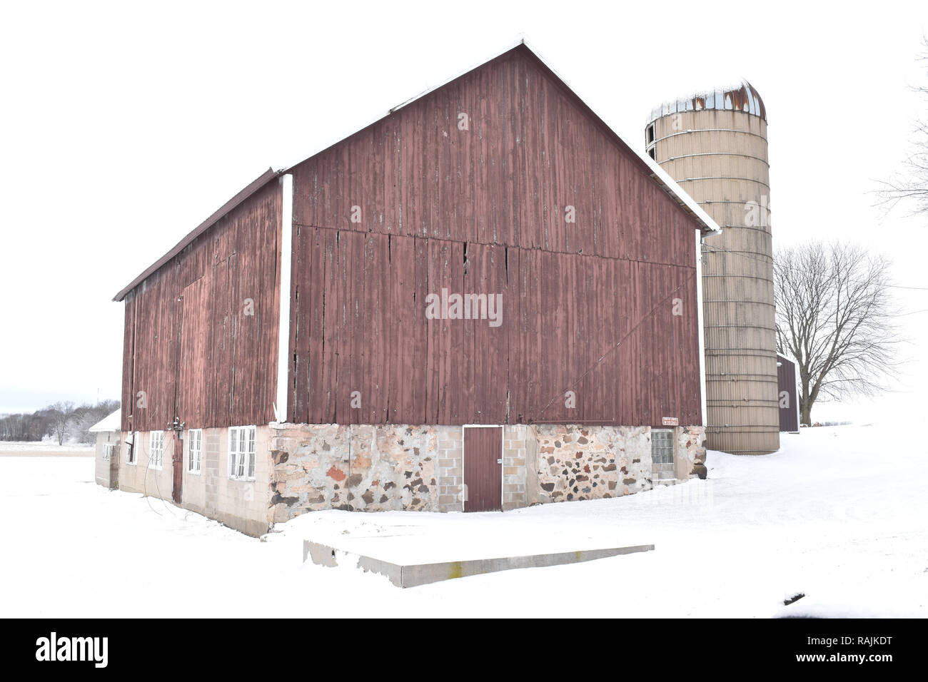 Vintage style red barn with field stone foundation and cement silo on a farm in a rural area in winter USA Stock Photo