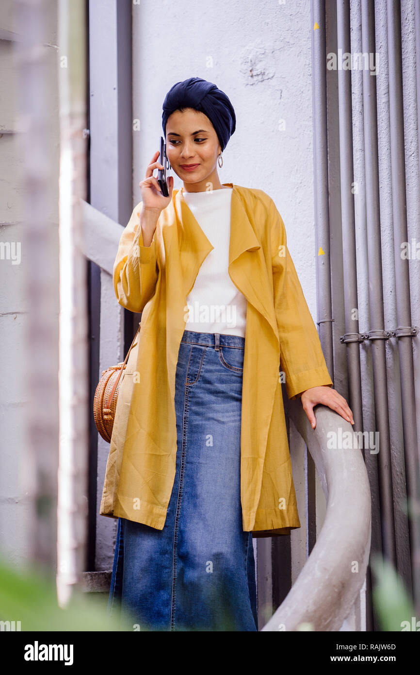 Portrait Of A Young And Beautiful Malay Muslim Woman In A Headscarf Turban Smiling As She Speaks To A Friend On Her Smartphone In A Garden In The Day Stock Photo