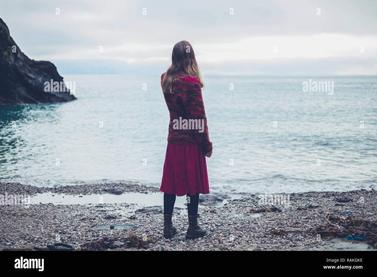 A young woman is standing on the beach looking at the sea Stock Photo ...
