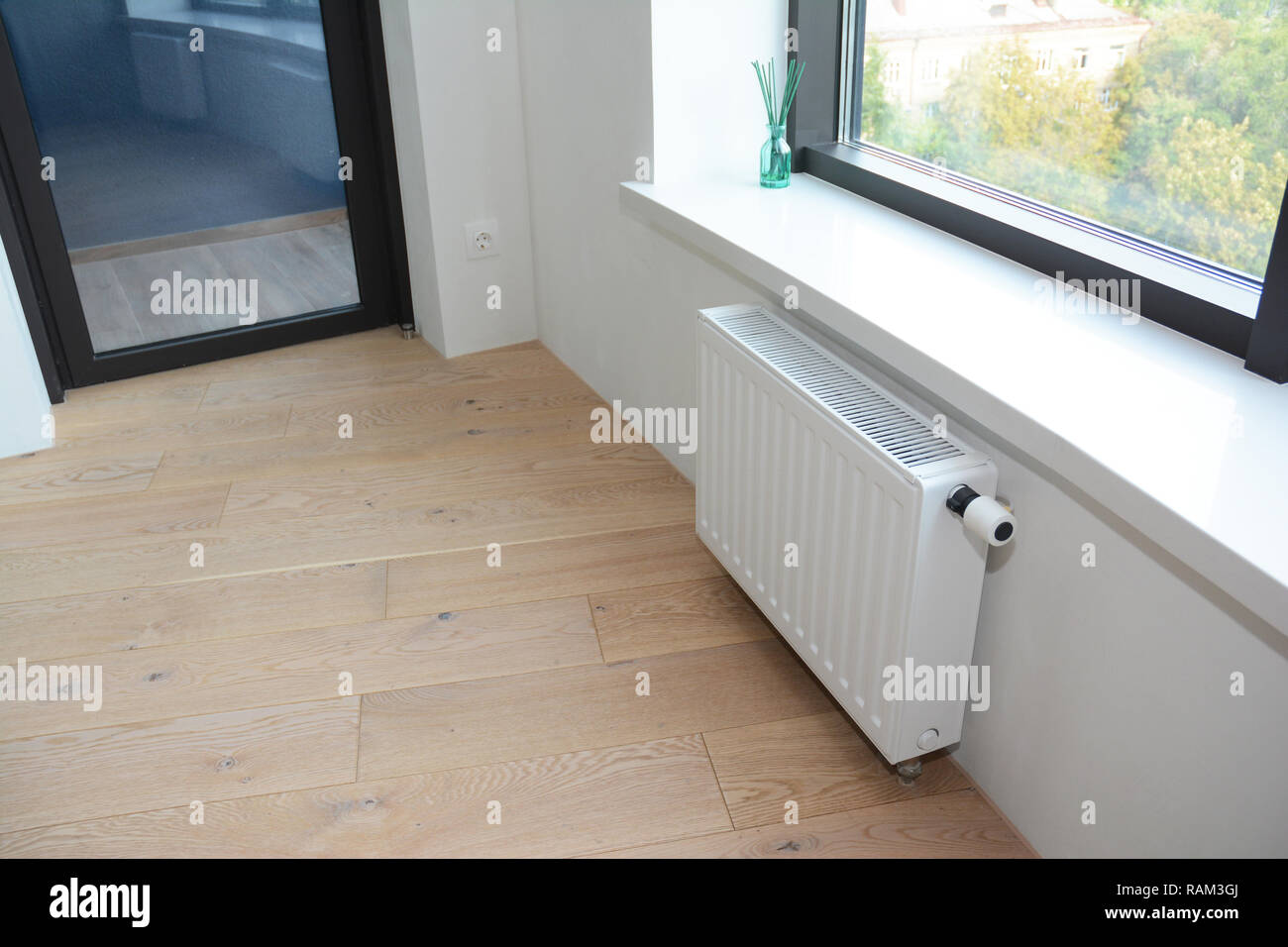White radiator heating with thermostat for energy saving in unfinished home room repair with balcony door. Stock Photo