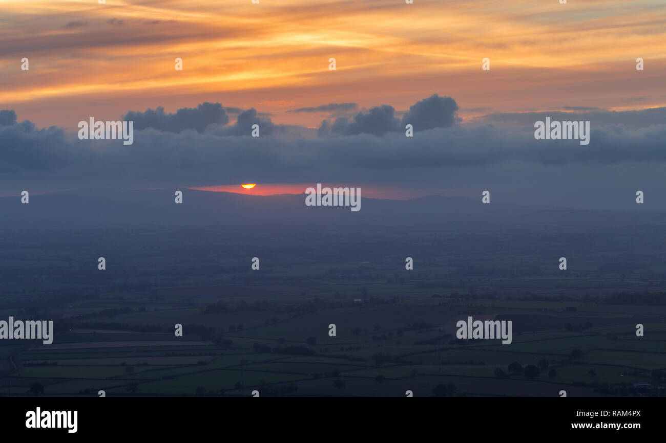 Aerial view over hazy fields of British countryside with orange setting sun over scenic hills Stock Photo