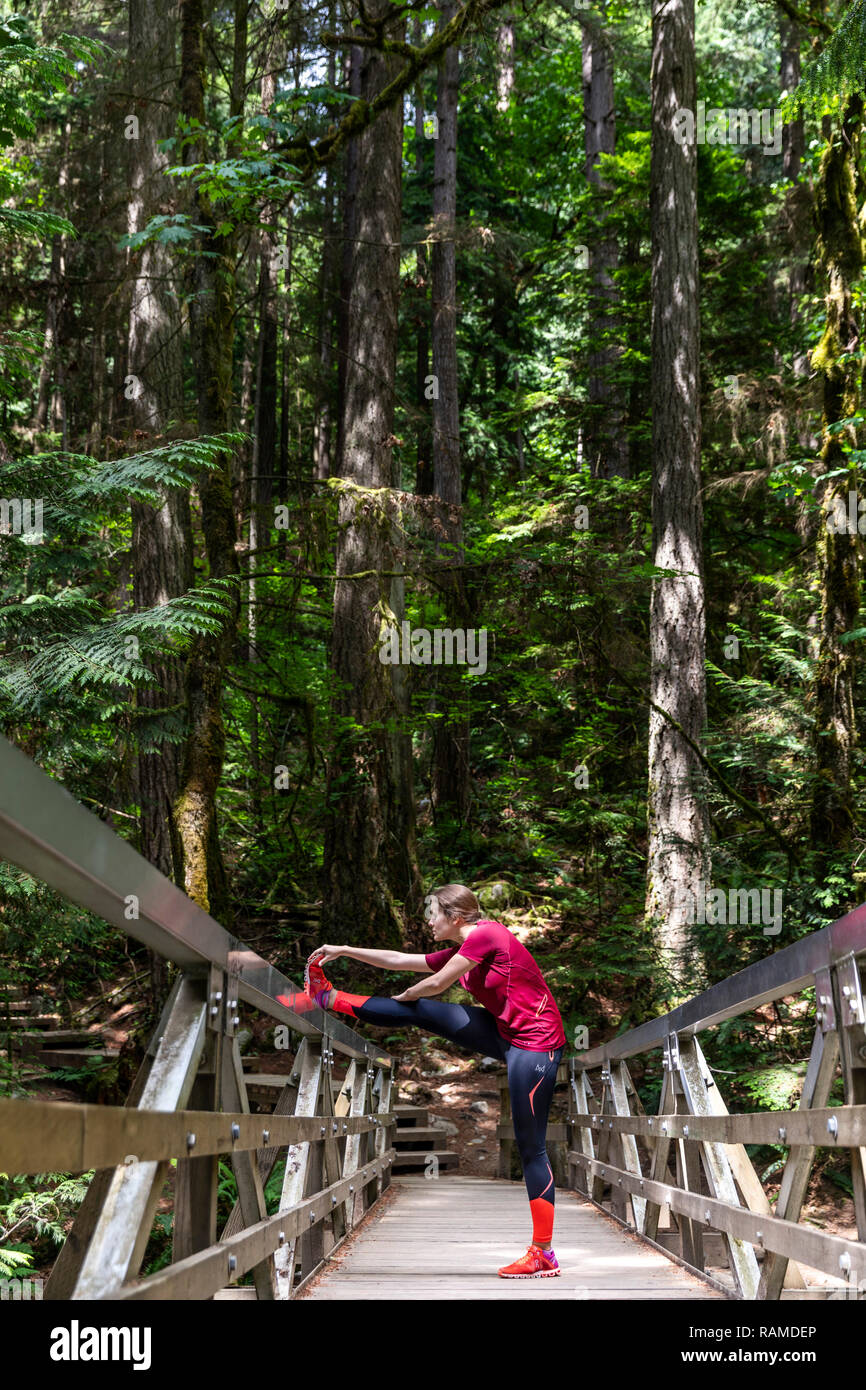 Girl stretching hamstrings in the bridge inside the forest of Deep Cove in Canada Stock Photo
