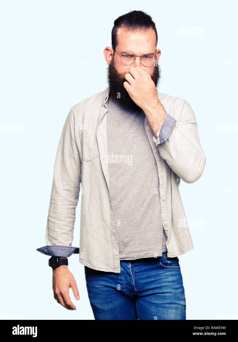 Young blond man wearing glasses smelling something stinky and