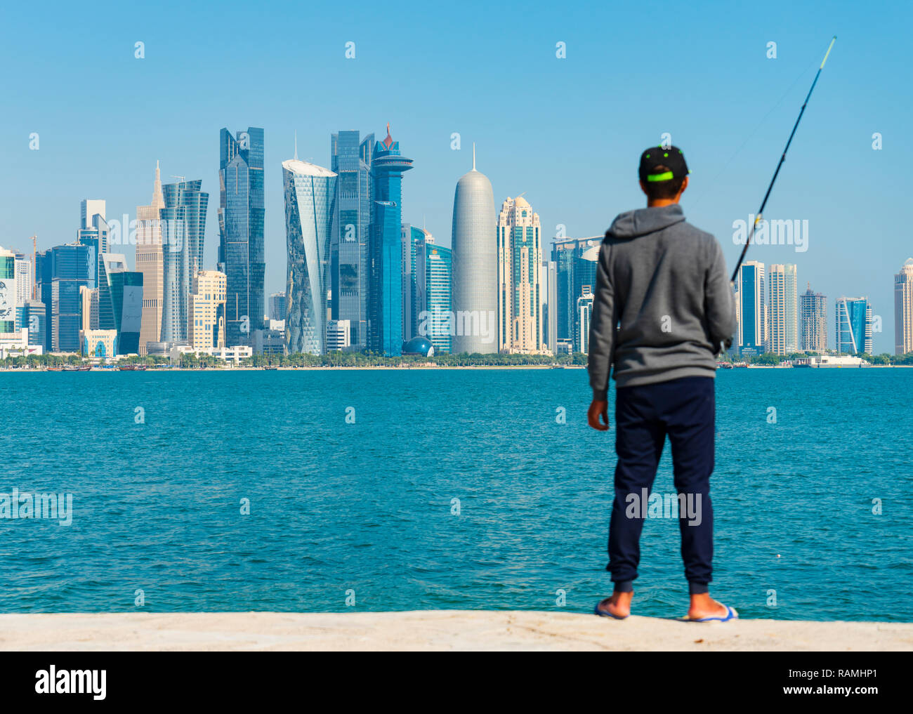 Man fishing from The Corniche and skyline view of West Bay business district from The Corniche in Doha, Qatar Stock Photo
