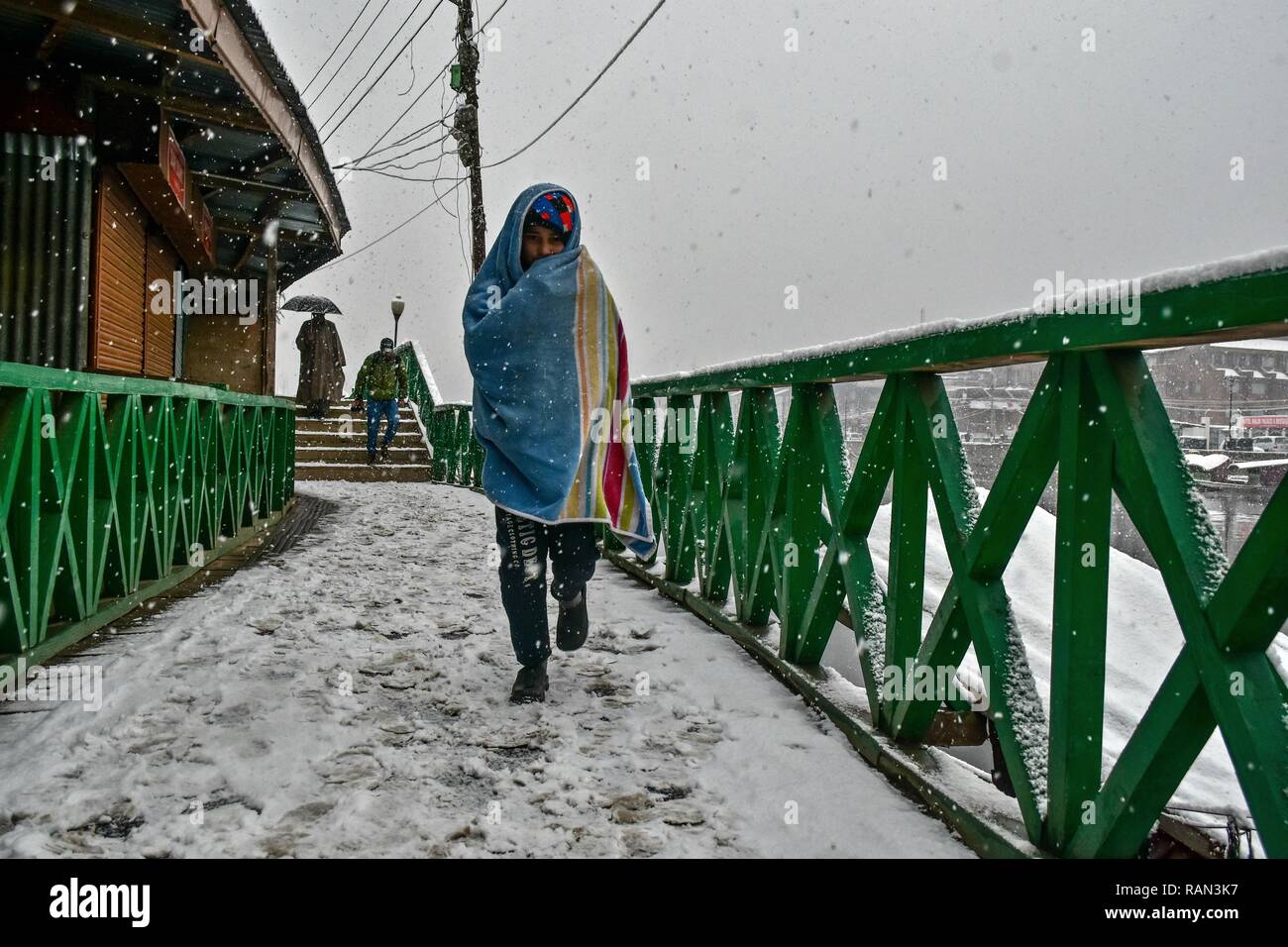 A resident seen walking through a snow covered street during snowfall. Kashmir received its first snowfall of the new year, breaking a month-long dry spell in the Valley. Srinagar recorded a 0 degrees Celsius -- an increase of over four degrees from minus 4.2 degrees Celsius on the previous, the Met department said. The weather department has predicted more snowfall in Kashmir over the next three days. Stock Photo