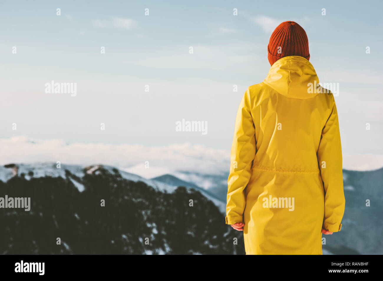 Woman exploring mountains adventure travel lifestyle winter vacations outdoor girl standing alone wearing yellow raincoat Stock Photo