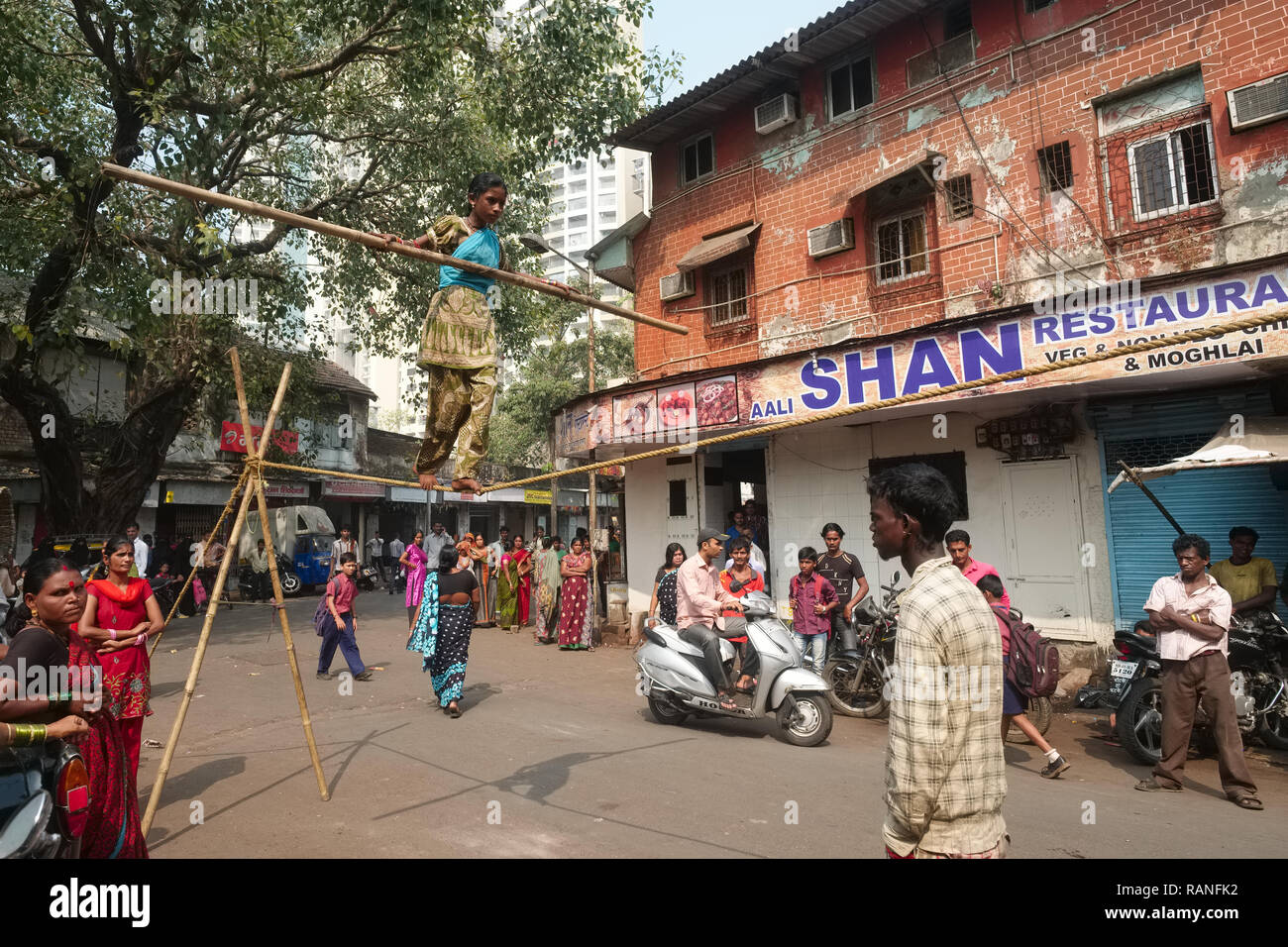 In a 'tamasha' in Foras Rd., Mumbai, India, a street show, a girl performs a tightrope act, observed by her handler (r) and street prostitutes Stock Photo