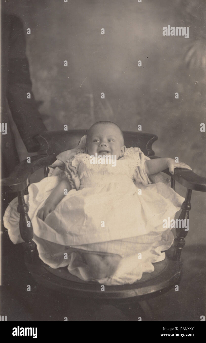 Vintage Photographic Postcard of a Baby Laughing Whilst Laying in a Chair Stock Photo