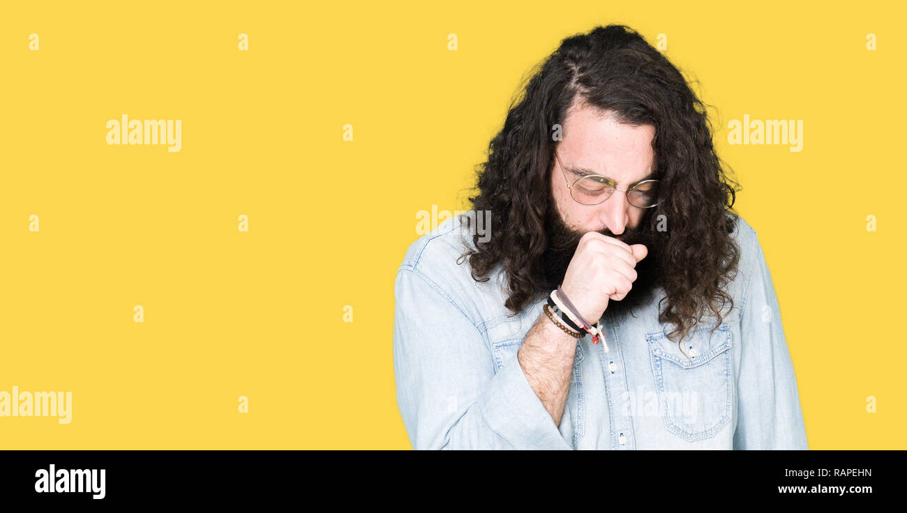 Young hipster man with long hair and beard wearing glasses feeling unwell and coughing as symptom for cold or bronchitis. Healthcare concept. Stock Photo
