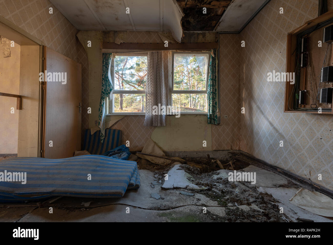 Prerow, Germany - December 30, 2018: View of an old mattress, floral wallpaper and curtains of a room in a barrack of the former training camp of the  Stock Photo