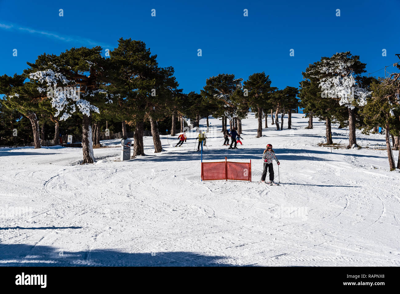 Navacerrada, Spain - December 7, 2017: Skiers skiing downhill in ski resort in Guadarrama mountain range at winter time a sunny day with blue sky Stock Photo