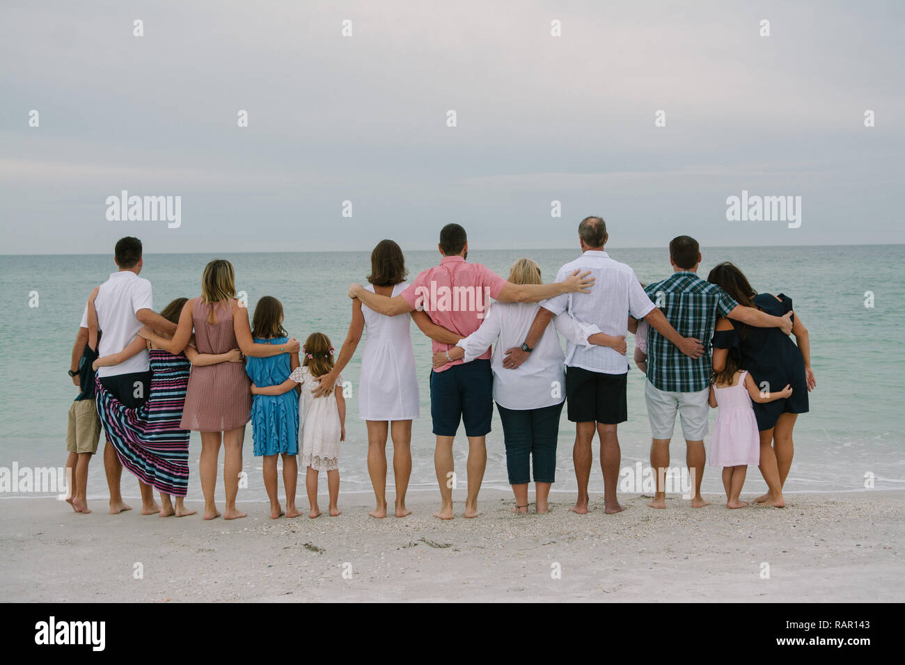 Huge Happy Traveling Caucasian Family with Adults and Kids at the Beach Hugging while facing the Ocean Horizon Outside on Destination Vacation Stock Photo
