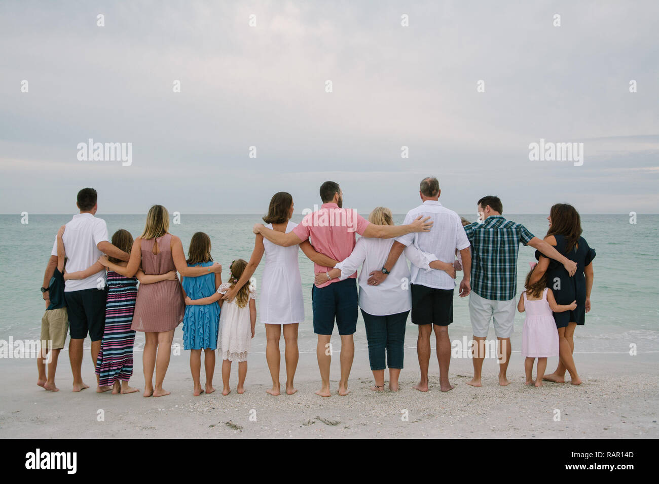 Huge Happy Traveling Caucasian Family with Adults and Kids at the Beach Hugging while facing the Ocean Horizon Outside on Destination Vacation Stock Photo