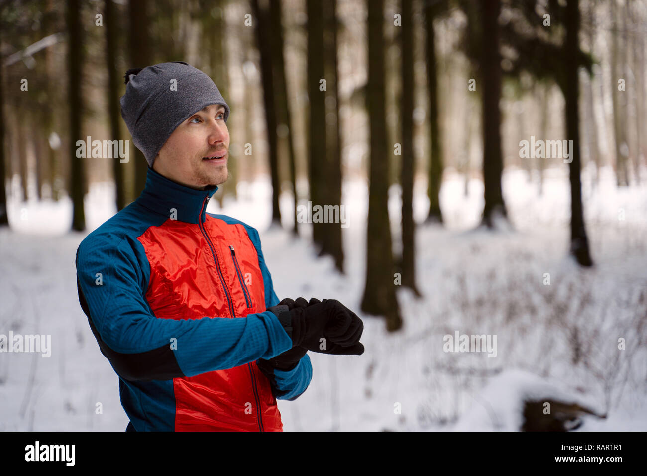 Runner wearing warm sporty clothes looks at a modern smart clock and counts up spent calories during winter training outdoors Stock Photo