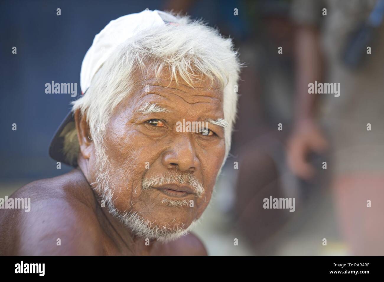 A village chief looks at the camera while sorting and dividing humanitarian supplies for equal distribution among his people during Operation Christmas Drop, Dec. 10, 2018, on Fais Island, Federated States of Micronesia. OCD is a humanitarian aid and disaster relief training exercise designed to not only provide remote un-surveyed airdrop training for aircrew, enhancing HA/DR response capabilities, but also provides over 60,000 pounds of humanitarian aid and supplies to 56 remote Pacific islands that rarely have contact for or access to regular supplies. Stock Photo