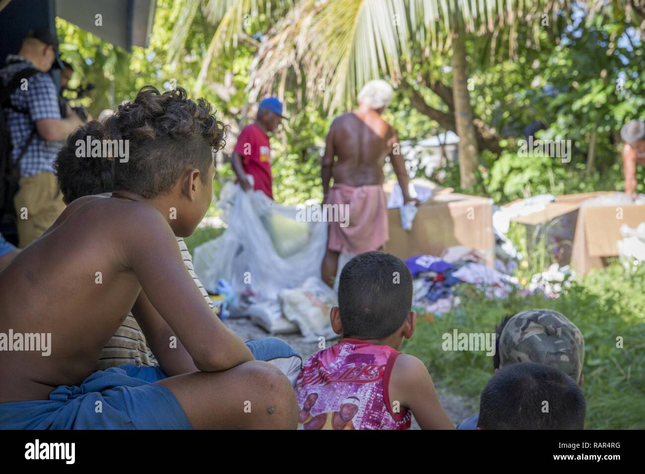 Island children wait and watch while their village chiefs sort and divide humanitarian supplies for equal distribution during Operation Christmas Drop, Dec. 10, 2018, on Fais Island, Federated States of Micronesia. Although Fais has a small airstrip, the islanders rarely get visitors, mail, or supplies, and look towards OCD each year for the resupply of clothing, fishing, educational, and medical supplies. Stock Photo