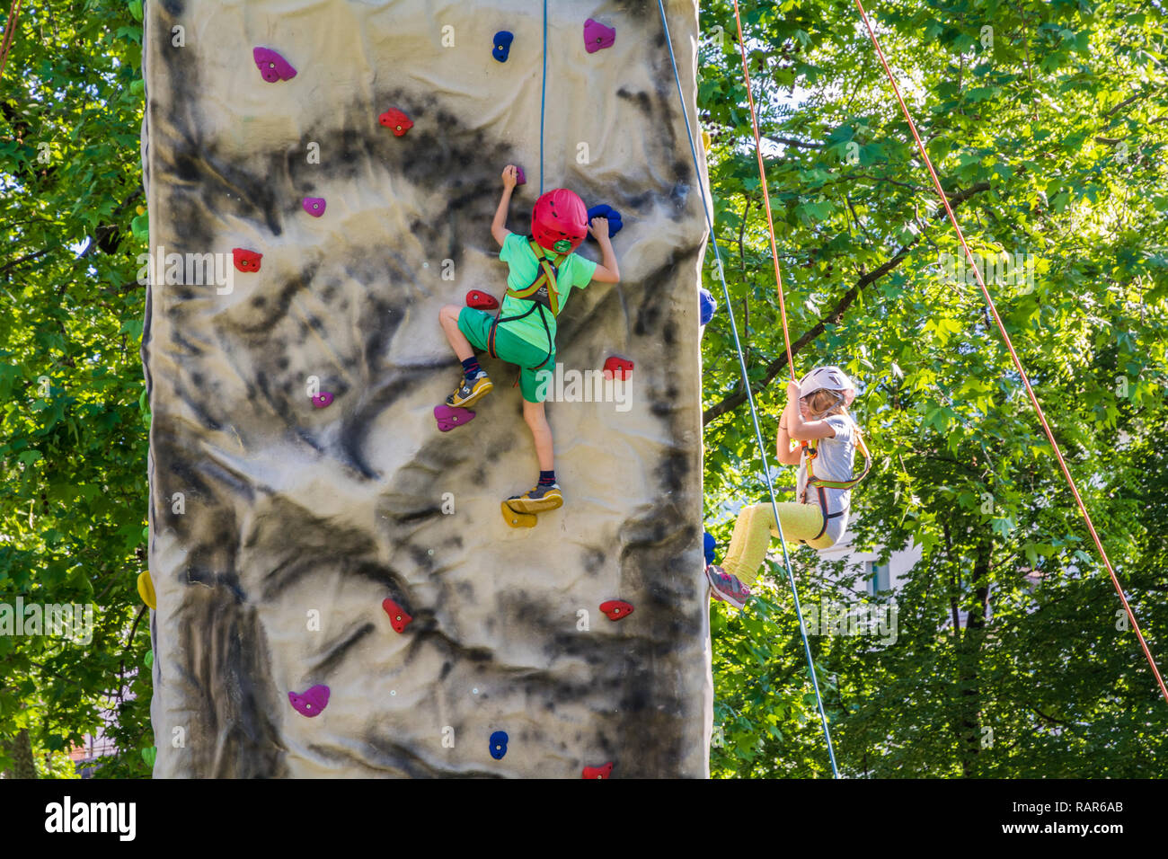 Children learning to rock climb on outdoor artificial climbing wall. Italy, north Italy, Europe Stock Photo