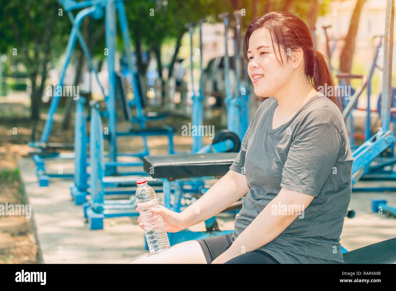 overweight woman drinking water after workout at outdoor park. Stock Photo