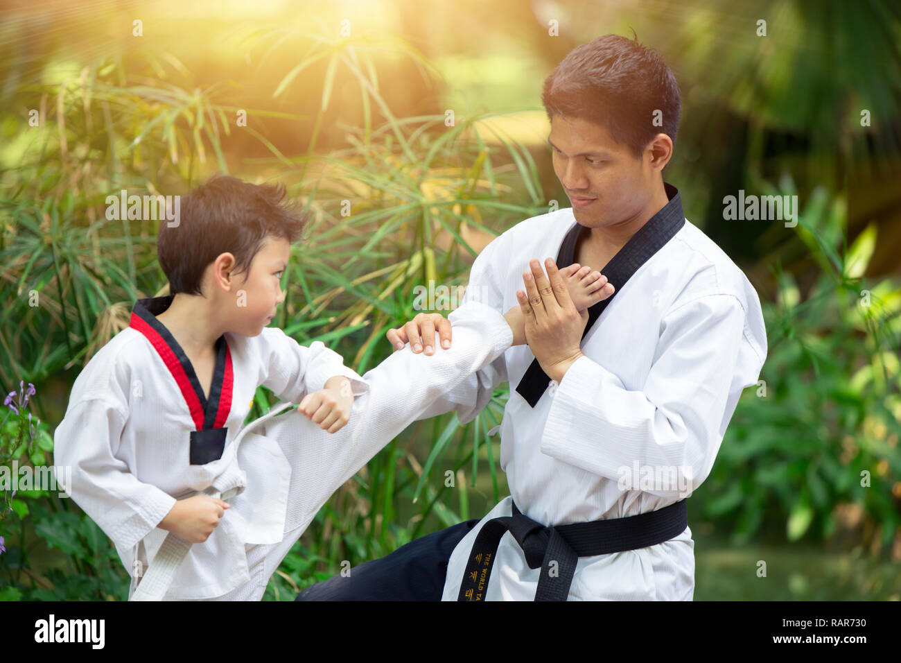 Boy and Dad enjoy healthy sport Taekwondo together outdoor for train fighter kick. Stock Photo