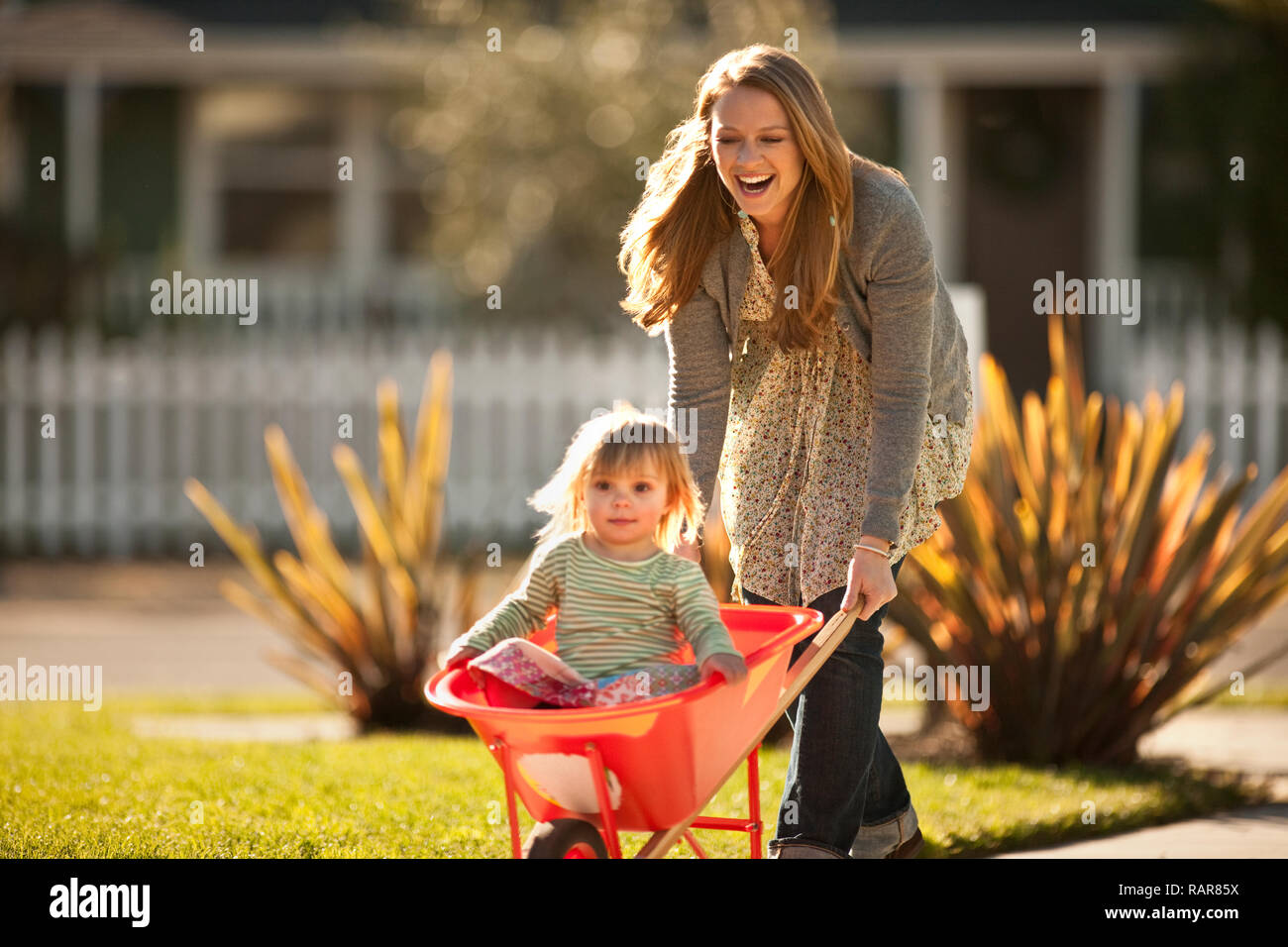 Woman pushing a wheelbarrow with her young daughter inside Stock Photo ...