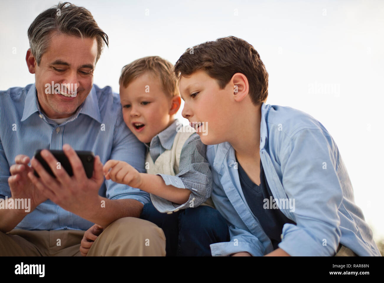 Mature man showing his cellphone to his curious sons. Stock Photo