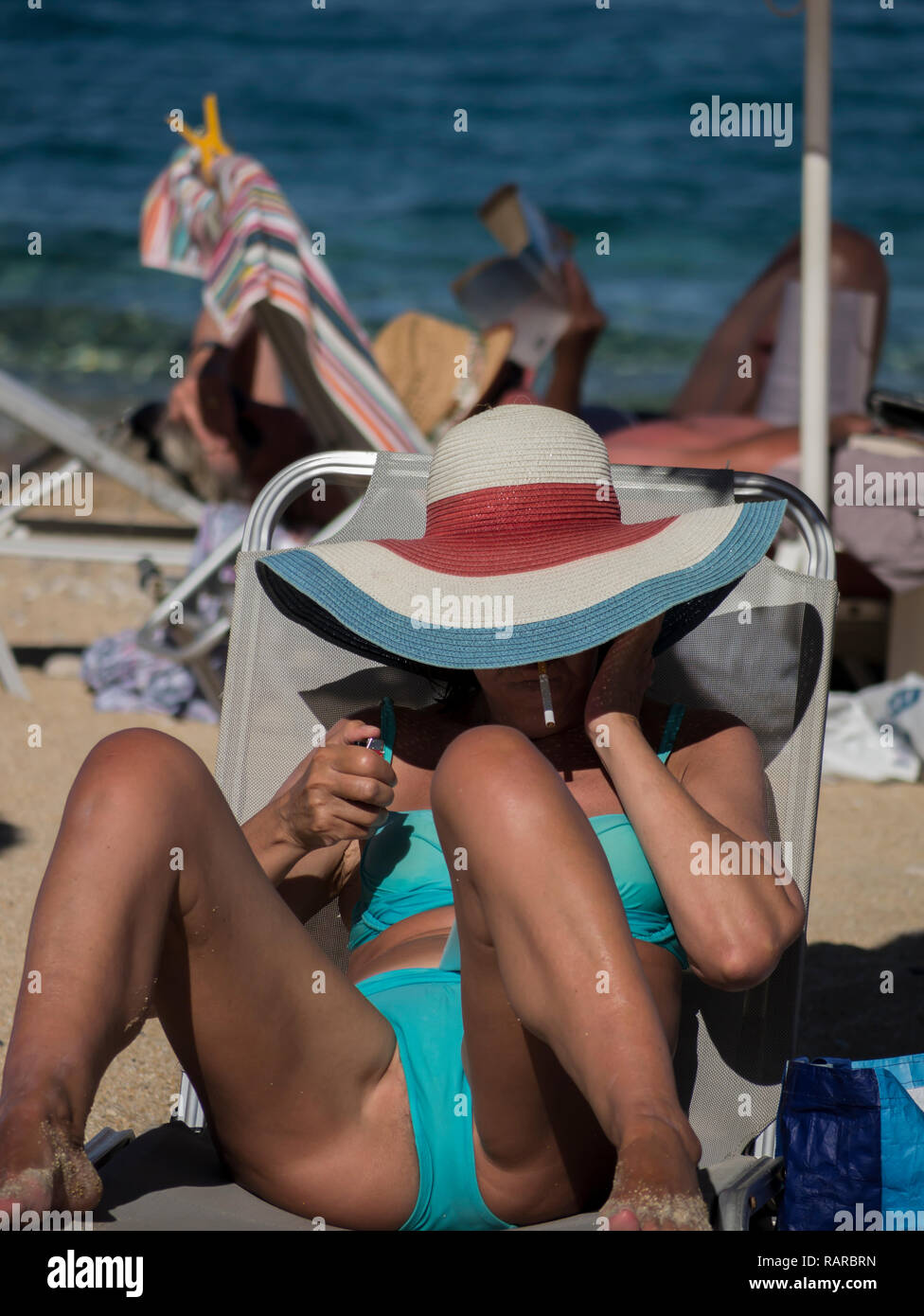 Woman on the beach wearing stylish hat smoking a cigarette Stock Photo