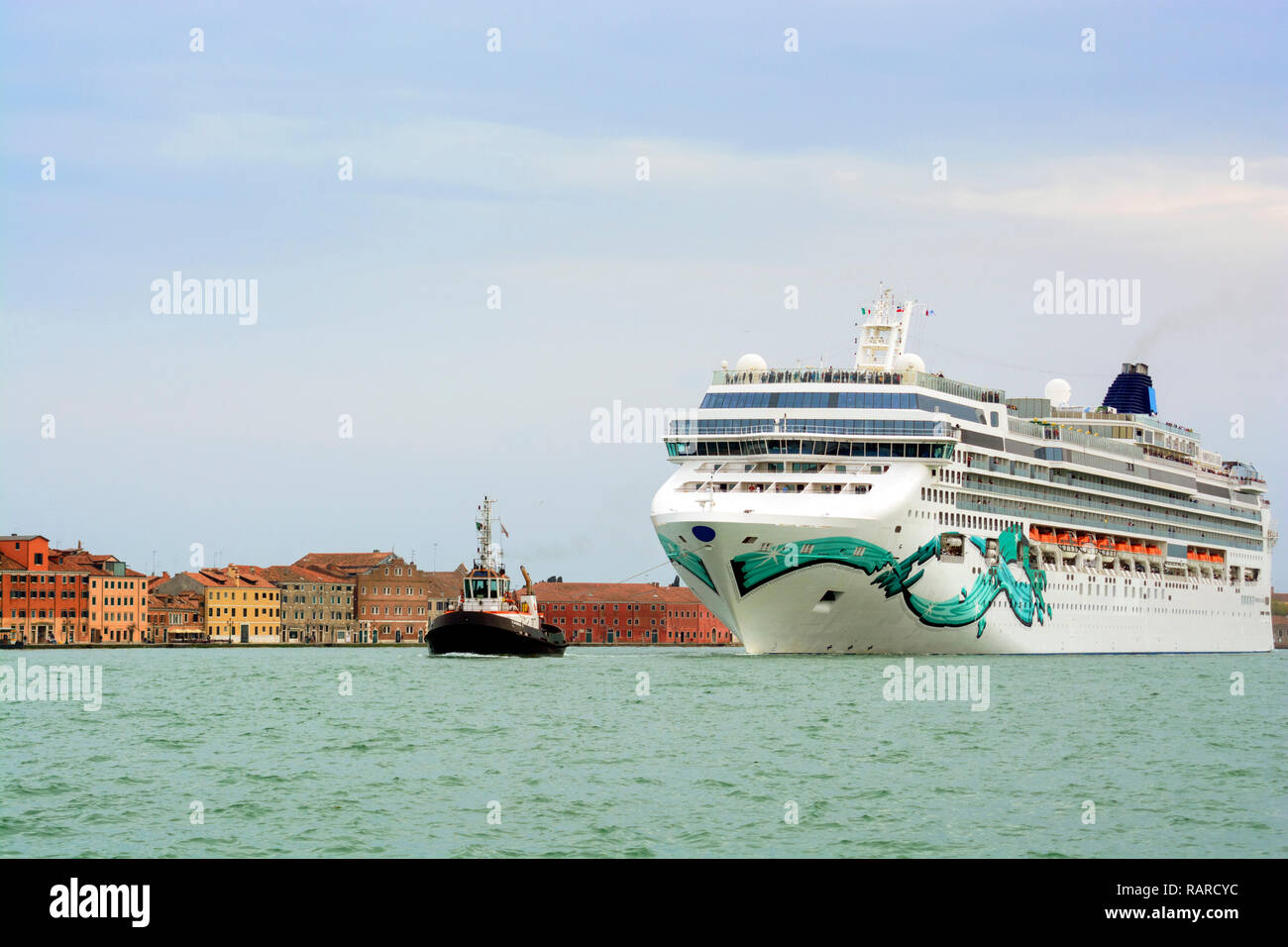 Small tugboat pulls a big cruise ship against row of old houses in Venice Stock Photo