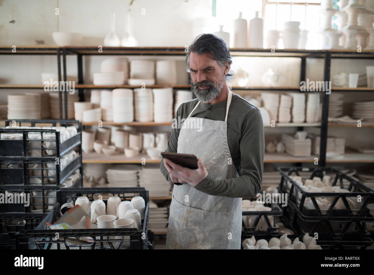 Focused potter using tablet surrounded by work Stock Photo
