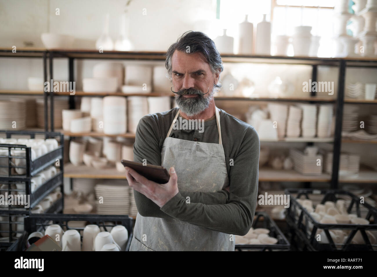 Serious potter using tablet surrounded by work Stock Photo