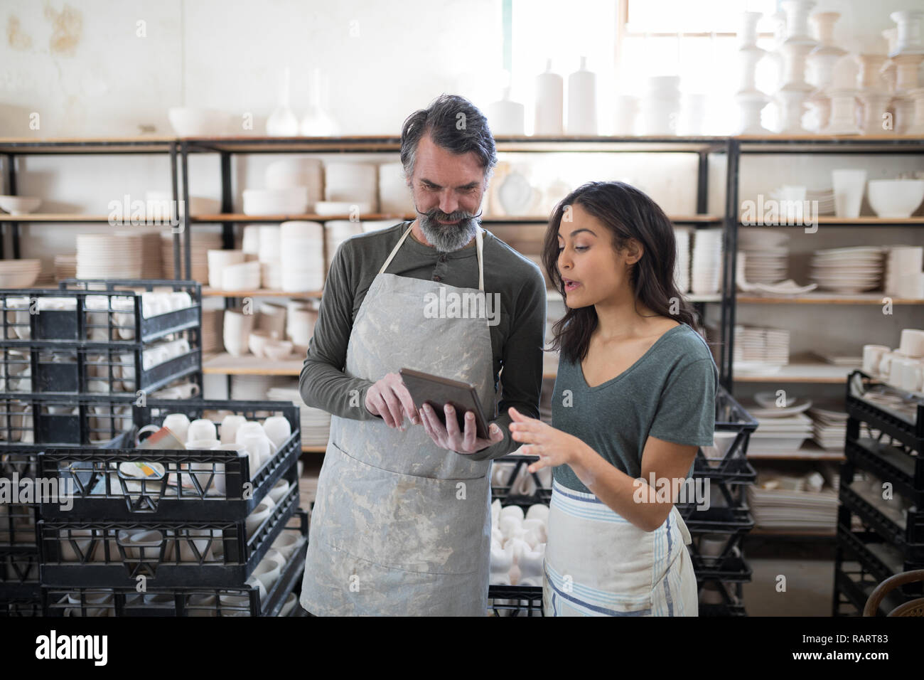 Smiling potter colleagues using tablet pc and talking Stock Photo