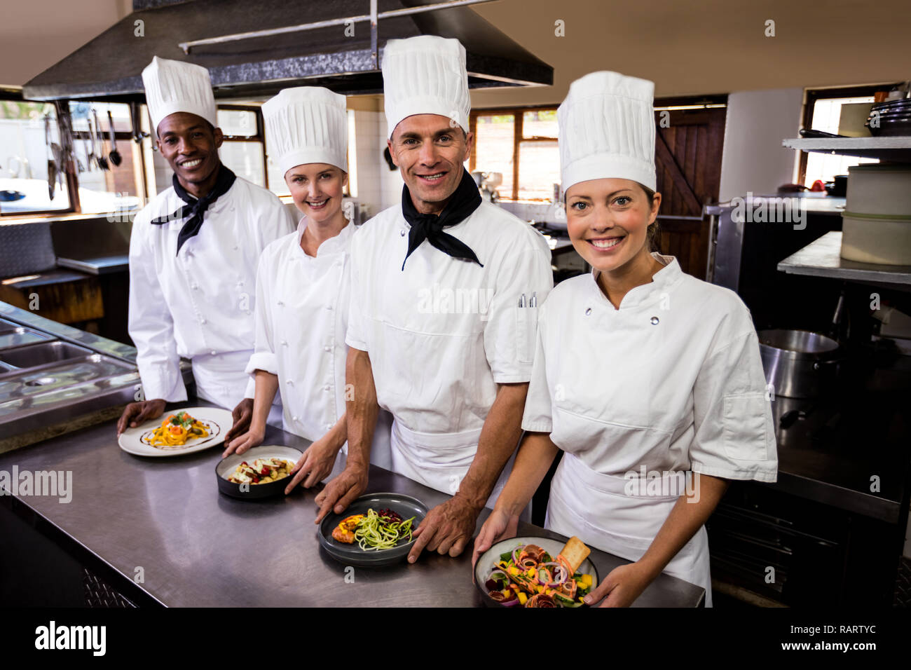 Group of chefs holding plate of prepared food in kitchen Stock Photo