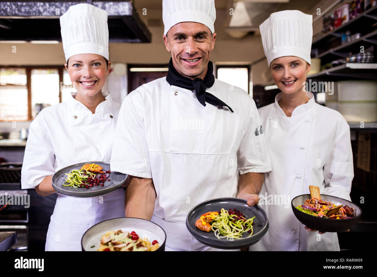 Group of chefs holding plate of prepared food in kitchen Stock Photo