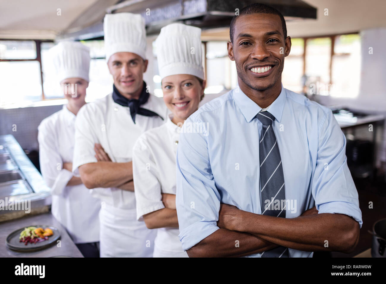 Group of chefs and manager standing with arms crossed in kitchen Stock