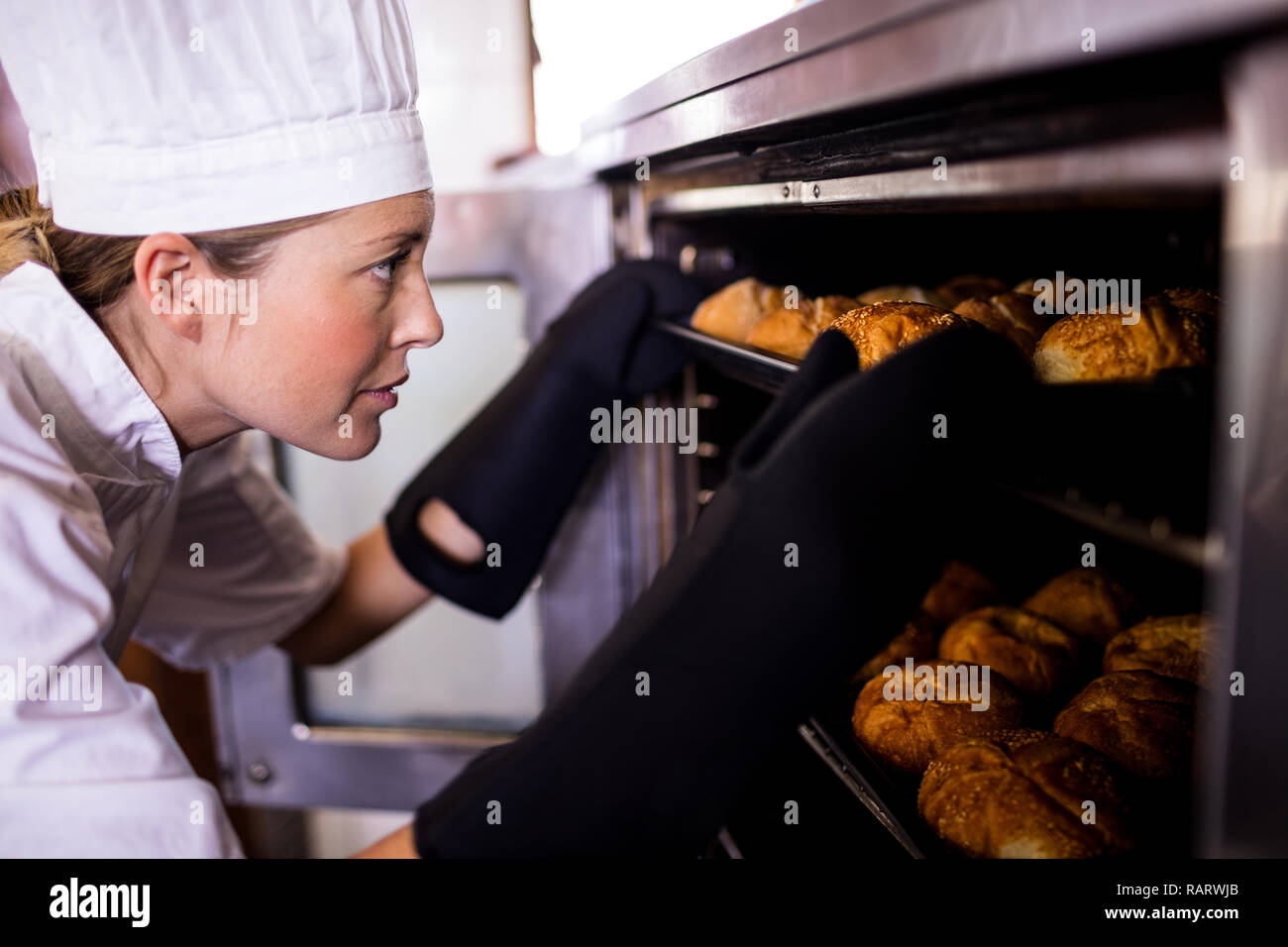 Female chefs putting baking tray of kaiser rolls in oven Stock Photo Alamy