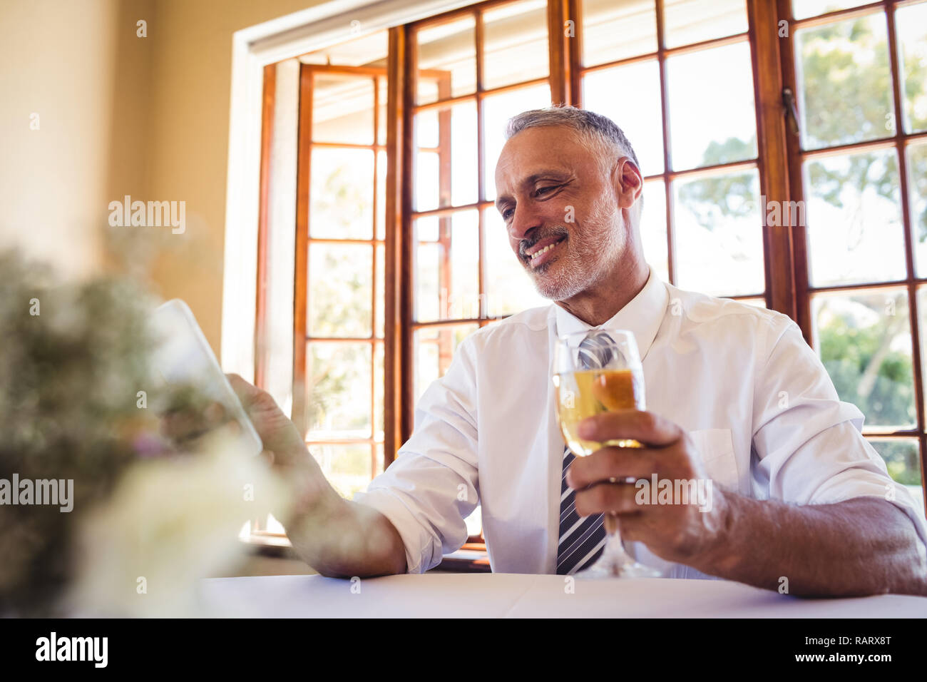 Businessman using mobile phone while having white wine Stock Photo
