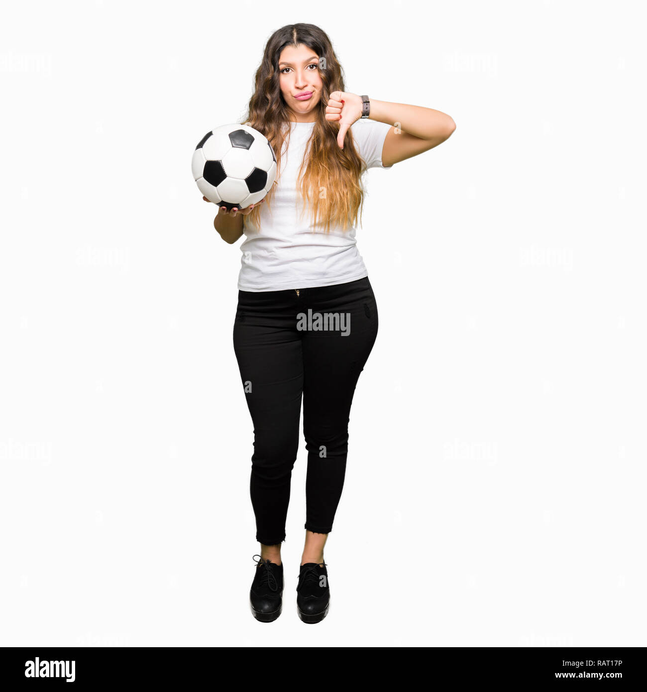 Young adult woman holding soccer football ball with angry face, negative sign showing dislike with thumbs down, rejection concept Stock Photo